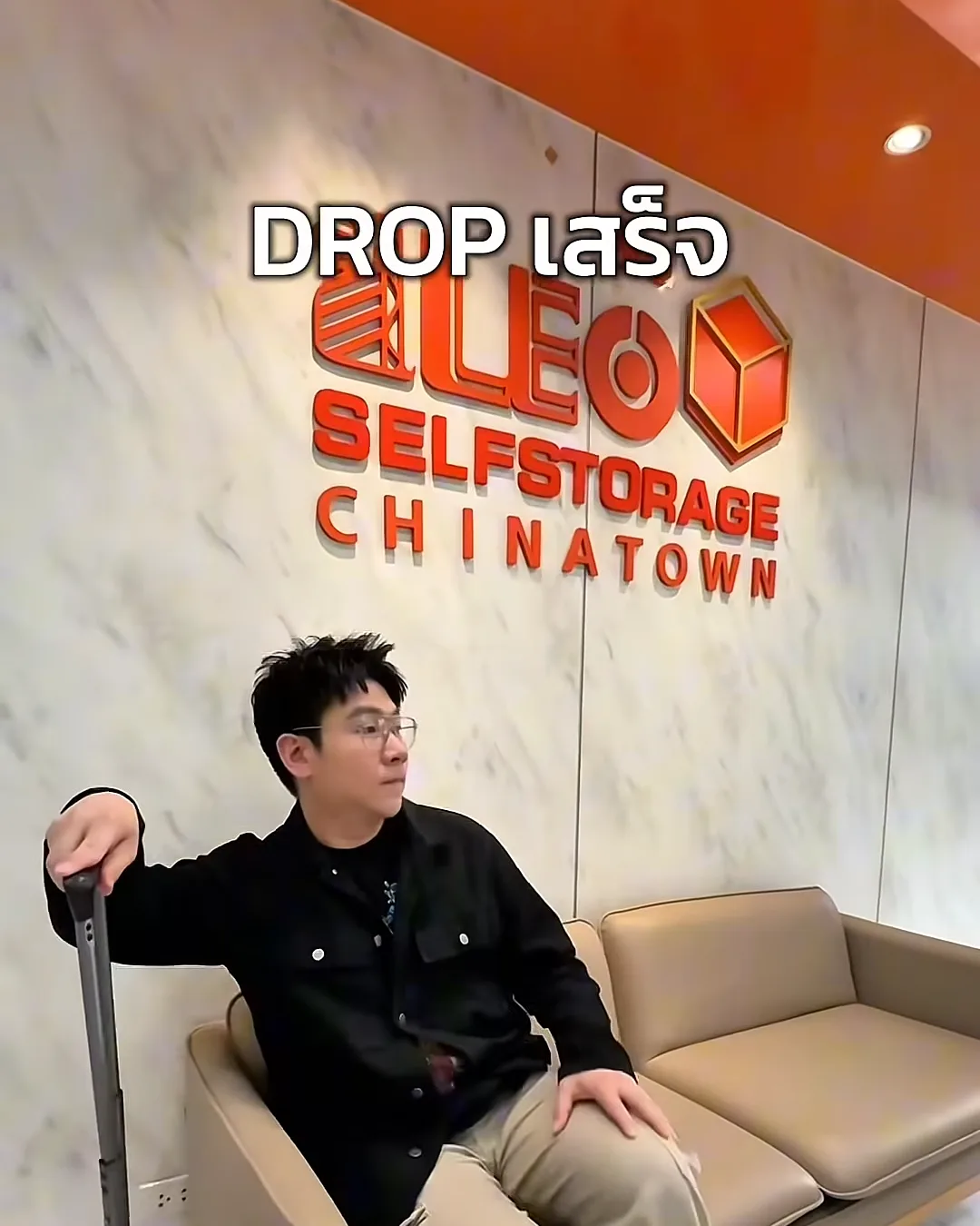 นั่งพักบนโซฟาหน้าโลโก้ LEO Self Storage Chinatown หลังดรอปกระเป๋าเสร็จ
