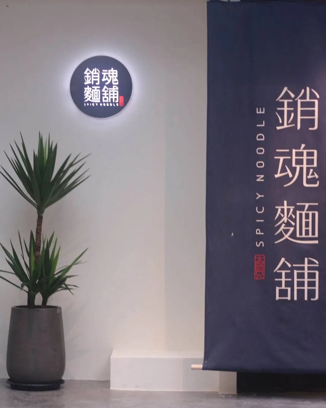 ผนังโลโก้ร้าน 銷魂麵舖 และผ้าม่านสีกรมท่าเขียน Spicy Noodle ภายในร้าน