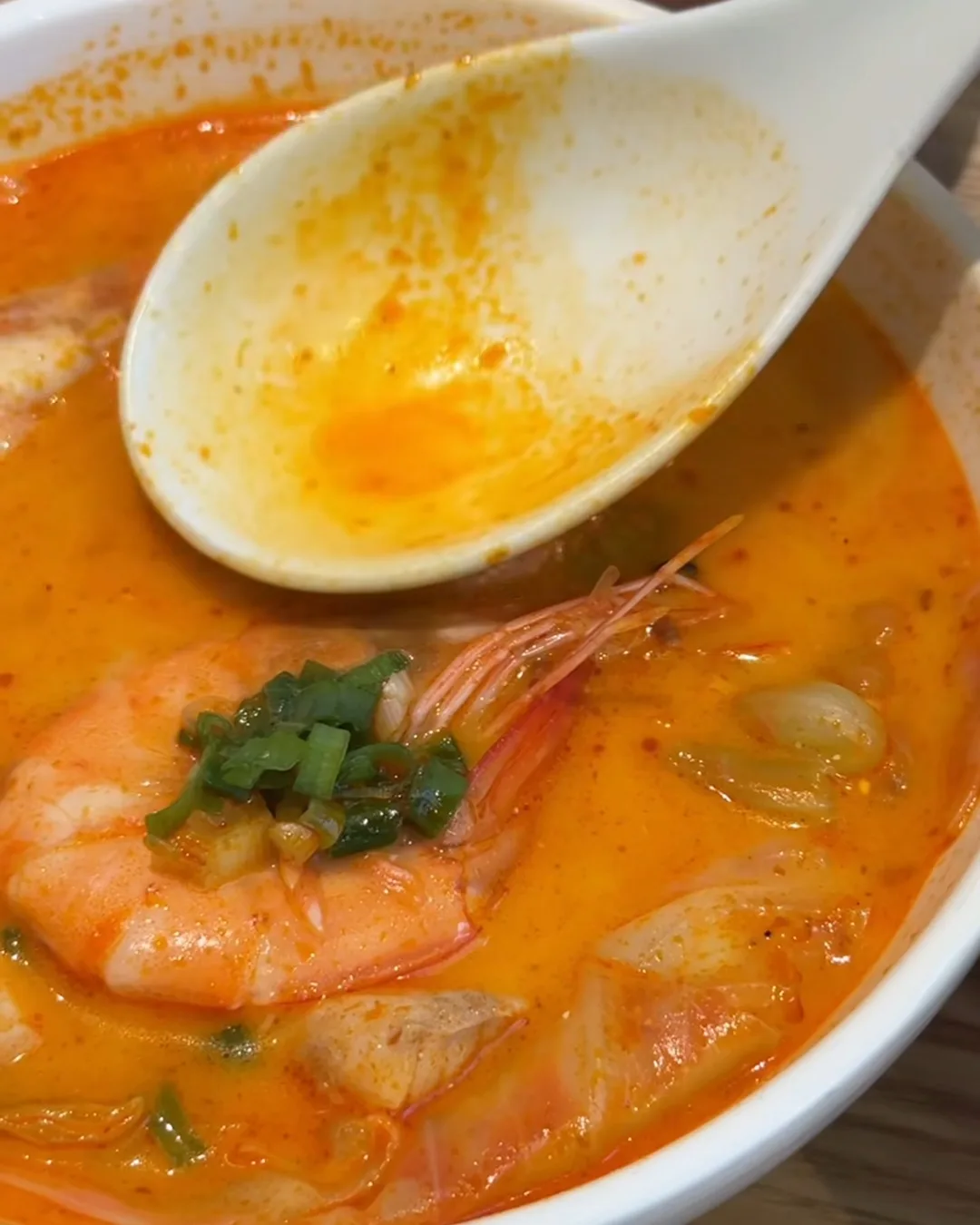 ซุปกุ้งเข้มข้นสีส้มในถ้วยขาว มีกุ้งตัวโตและต้นหอมซอย ช้อนตักซุป
