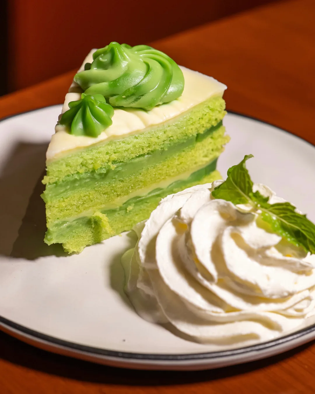 เค้กเปียกปูนสีเขียวใบเตยหลายชั้น ตกแต่งครีมสีเขียวบนจานขาว ร้านปูนแดงแกงร้อน