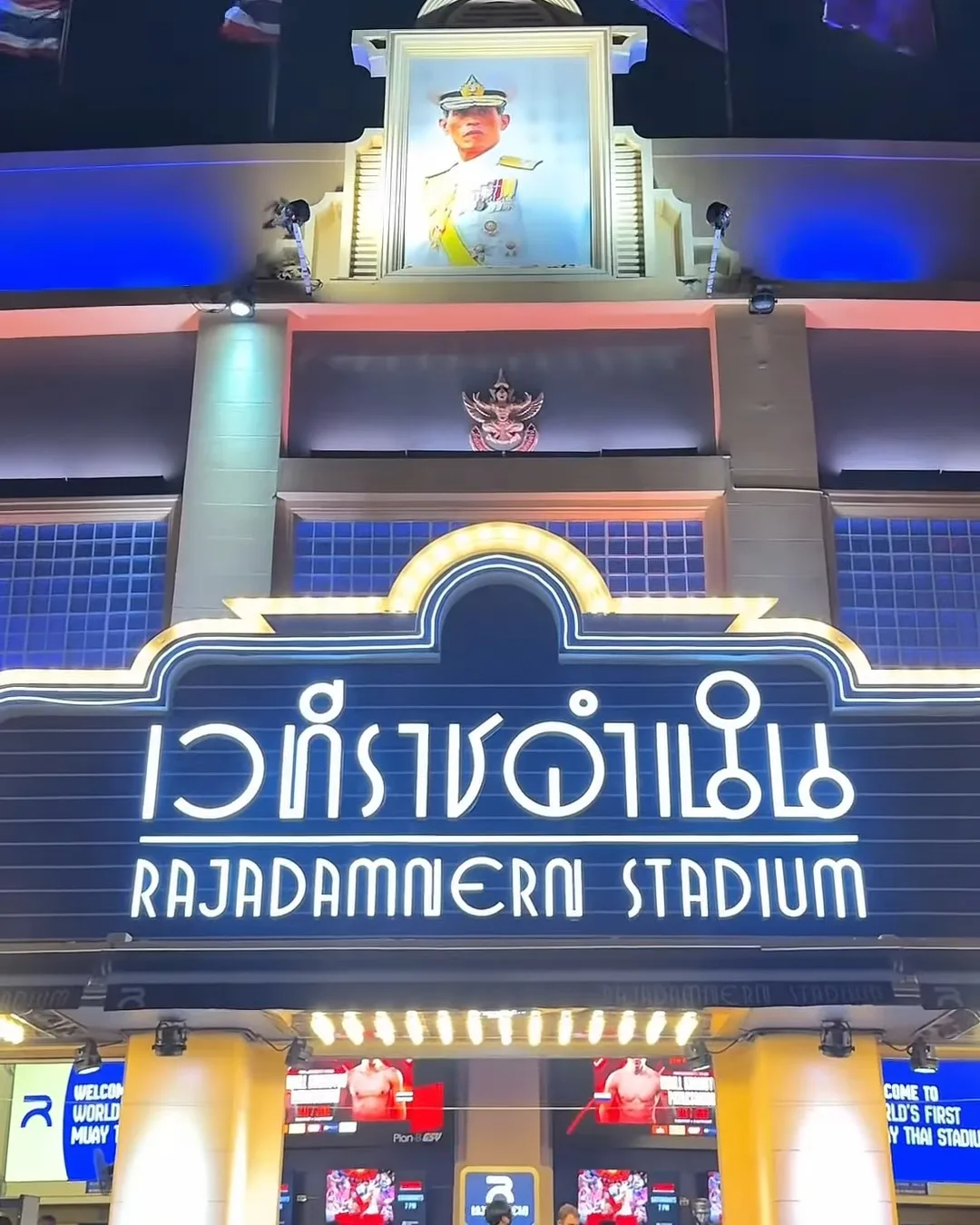 ป้ายไฟเวทีราชดำเนิน Rajadamnern Stadium เหนือทางเข้า ผู้ชมต่อคิวเดินขึ้นบันได