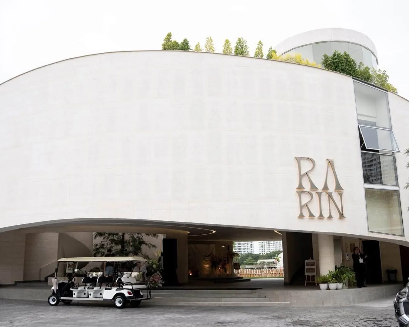 ด้านหน้าอาคาร RARIN สถานที่จัดงานแต่งงานราษฎร์บูรณะ ผนังโค้งสีขาวพร้อมโลโก้ RA RIN และรถกอล์ฟรับแขก