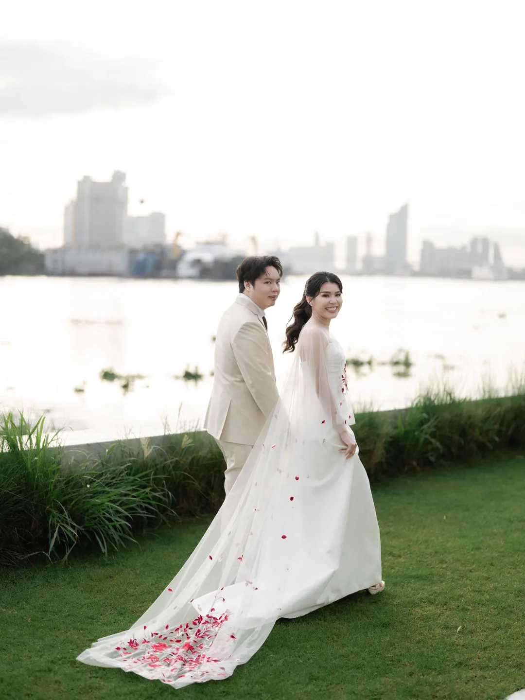 บ่าวสาวเดินจูงมือบนสนามหญ้าริมแม่น้ำเจ้าพระยา ชายกระโปรงโรยกลีบกุหลาบ