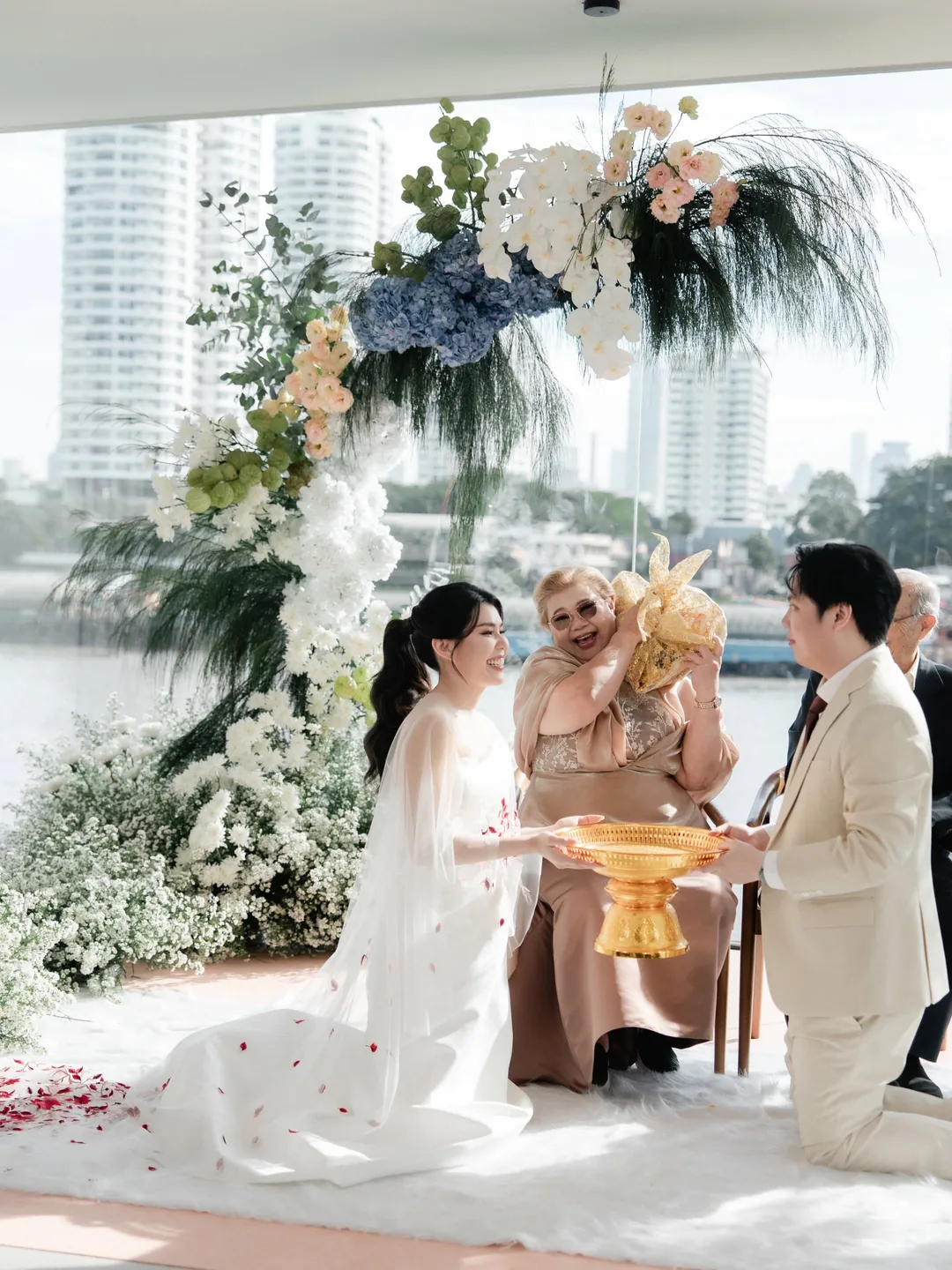 ผู้ใหญ่ส่งขันหมากให้บ่าวสาวในพิธีหมั้นที่ RARIN ซุ้มดอกไม้สีขาวและฟ้า