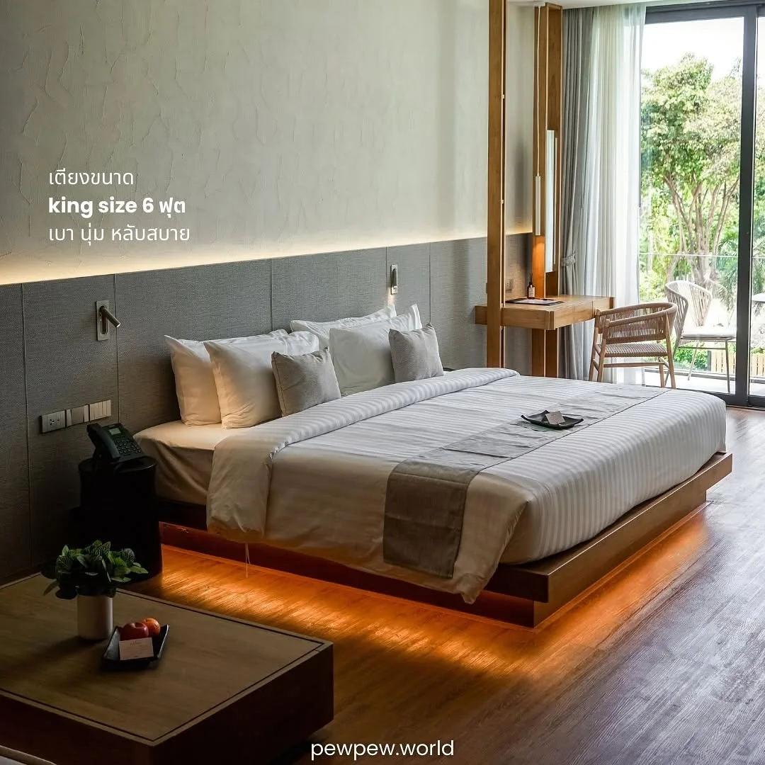 เตียงคิงไซซ์ 6 ฟุต ผ้าปูสีขาวเทา ไฟซ่อนใต้เตียงโทนส้ม ในห้อง Deluxe โรงแรม Riva Vista เชียงราย