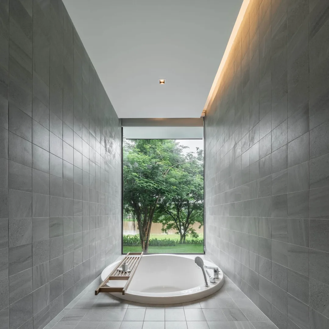 อ่างอาบน้ำทรงกลมกลางห้องน้ำผนังหินสีเทา หน้าต่างยาวมองเห็นต้นไม้ ที่ Riva Vista