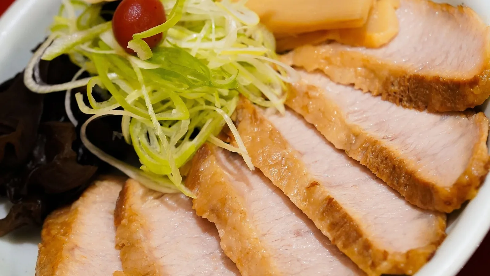 หมูชาชูแก้มหมูหั่นชิ้นเรียงบนจาน ต้นหอมซอย บ๊วยดอง และหน่อไม้ ราเมงแก้มหมู Santouka