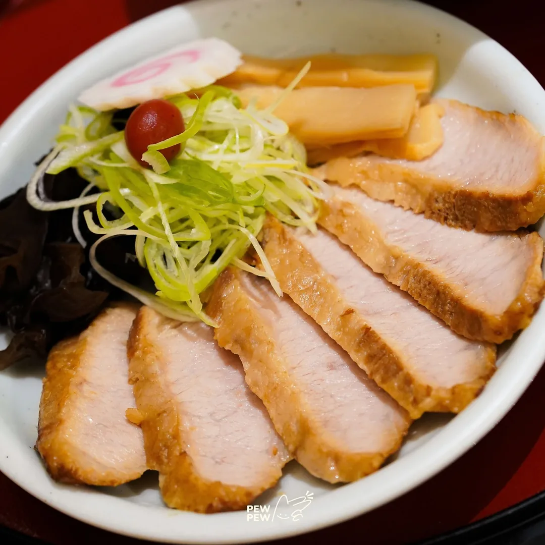 หมูชาชูแก้มหมูหั่นชิ้นบนจานขาว ต้นหอมซอย บ๊วยดอง นารุโตะ และหน่อไม้