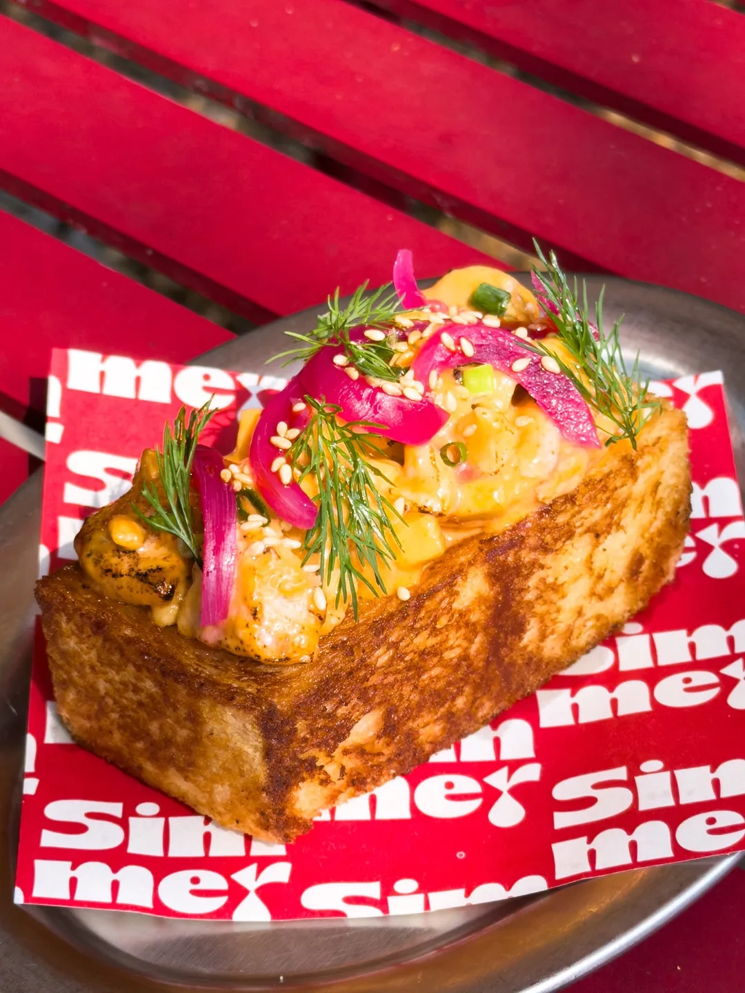 Shrimp Toast ขนมปังแผ่นหนาย่างกรอบ หน้ากุ้งซอสบิสก์ หอมแดงดอง และผักชีลาว บนกระดาษรองโลโก้ Simmer สีแดง