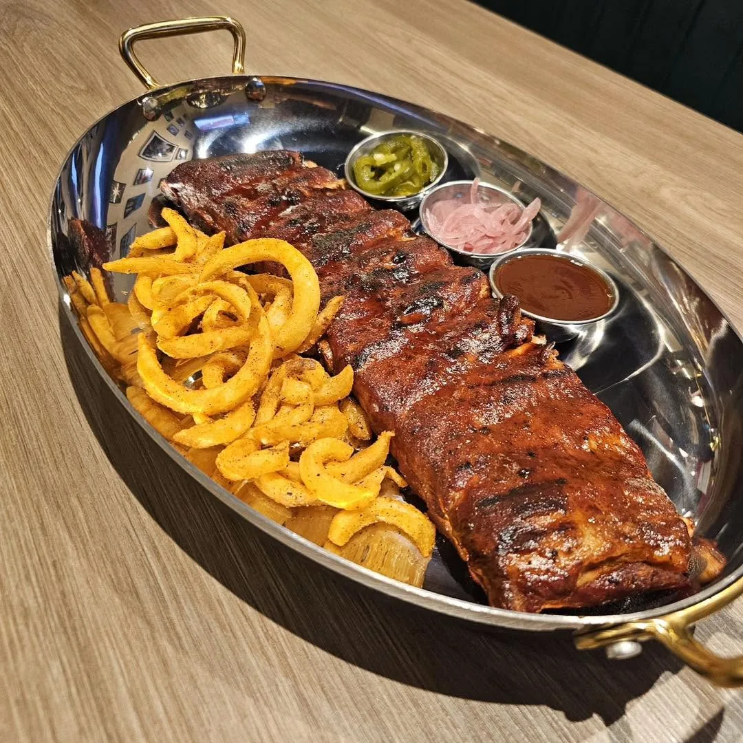 ซี่โครงหมูบาร์บีคิวในถาดสเตนเลสพร้อมเฟรนช์ฟรายส์และหัวหอมทอด