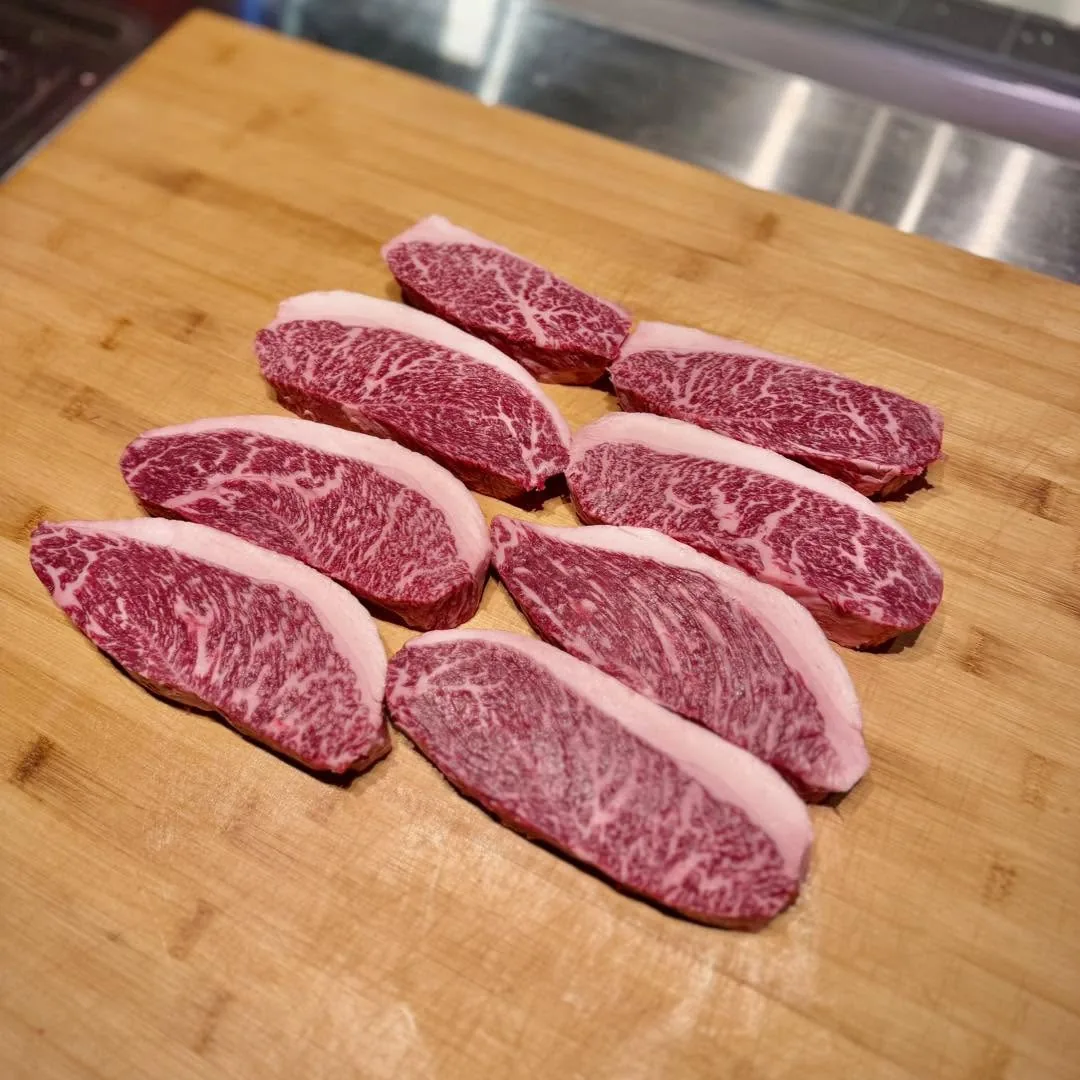 สเต็กเนื้อดิบหลายชิ้นวางเรียงบนเขียงไม้ เห็นไขมันแทรกชัด