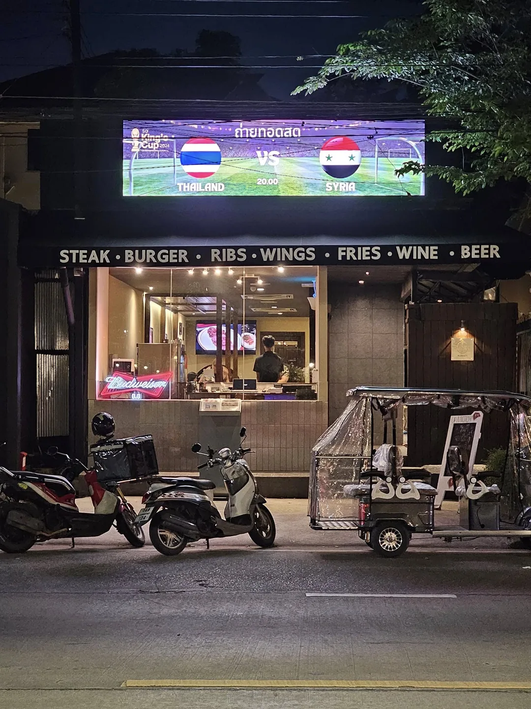 หน้าร้าน UP A NOTCH ลาดพร้าว 71 ตอนกลางคืน ป้าย STEAK BURGER RIBS WINGS FRIES WINE BEER และรถรับส่งจอดหน้าร้าน