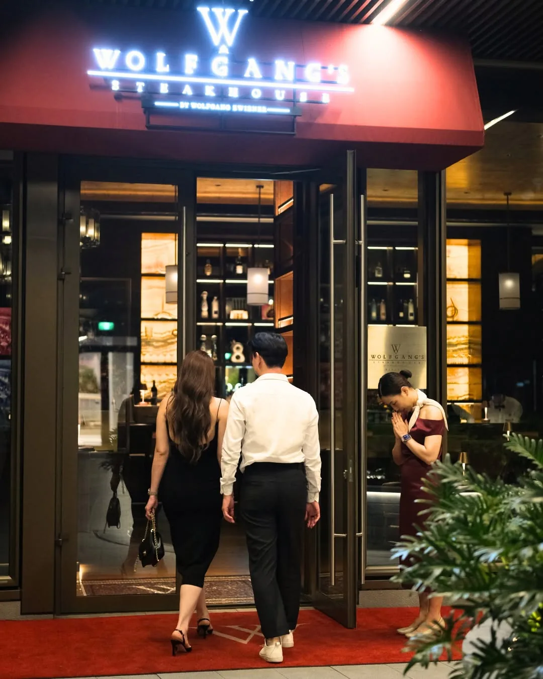 คู่รักเดินเข้าร้าน Wolfgang's Steakhouse ตอนกลางคืน
